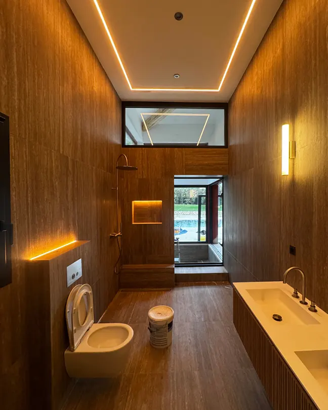 Luxury bathroom with continuous wood-grain tile, rain shower, cove lighting, and glass partition viewing outdoor pool