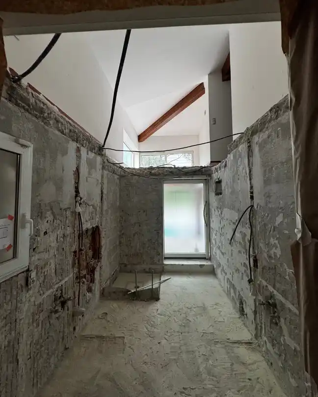 Bathroom renovation before photo showing gutted space with exposed concrete walls and ceiling structure
