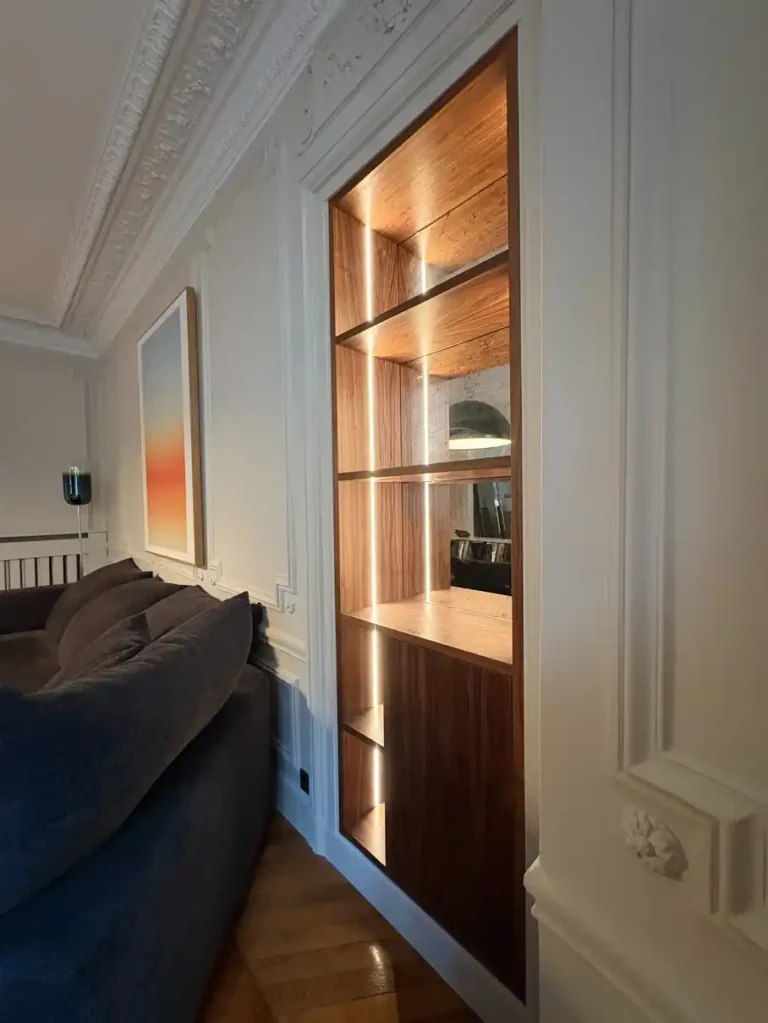 Elegant living room with custom LED-lit walnut shelving unit, ornate crown molding, and herringbone parquet flooring