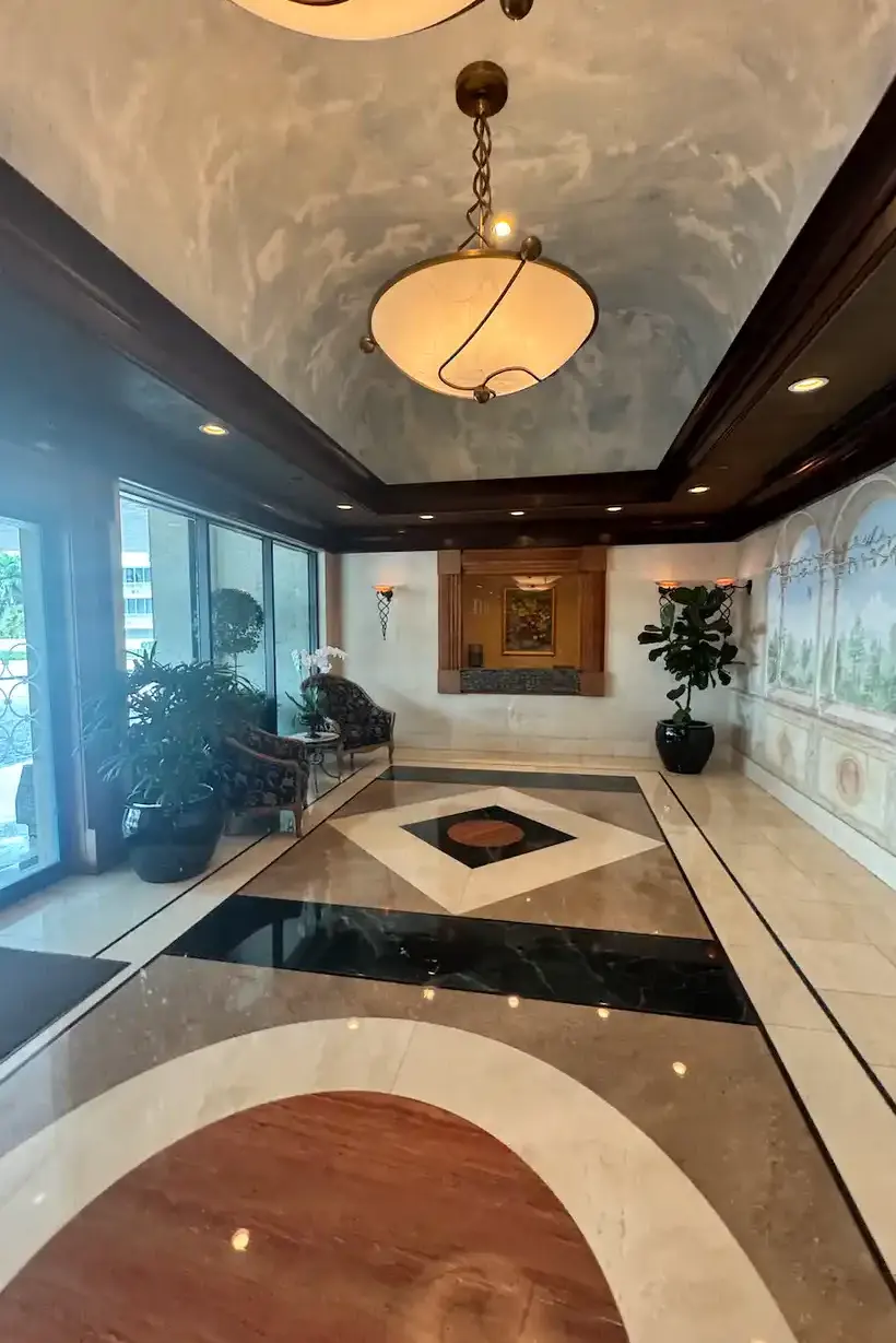 Grand hotel lobby featuring geometric marble floor patterns, sky-painted ceiling mural, dark wood molding, and traditional Persian area rug