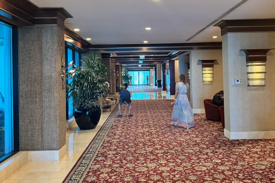 Hotel corridor with Persian runner carpet, dark wood columns, traditional wall sconces, and polished marble flooring